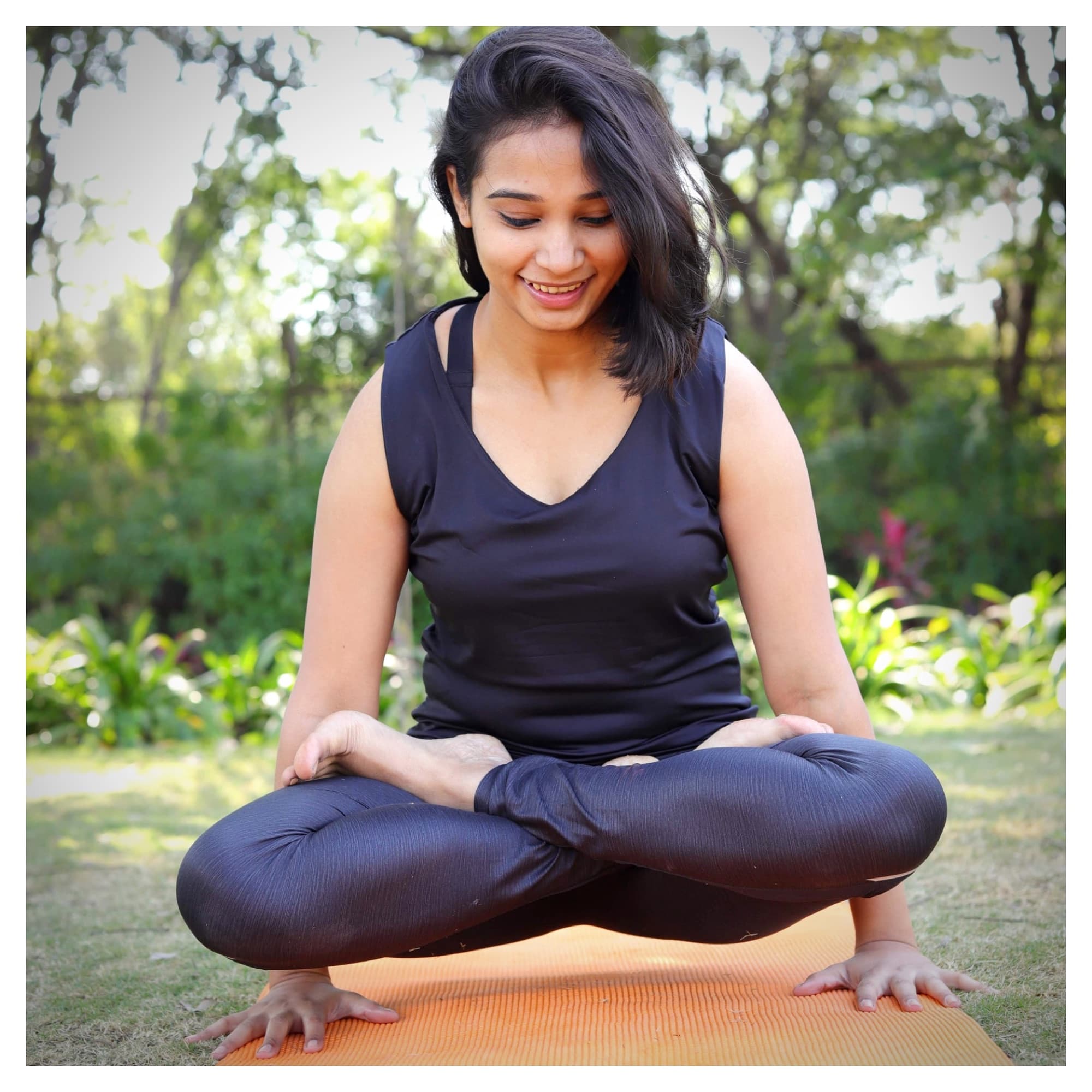 Devina seated cross-legged, smiling, in a garden